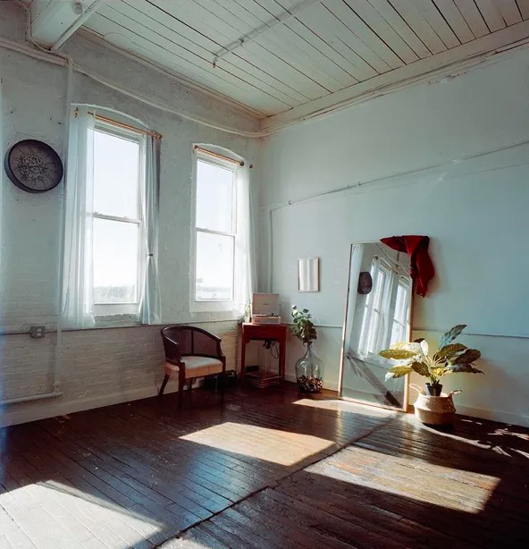 Sunlit artist studio with two tall arched windows, exposed brick and dark hardwood floors