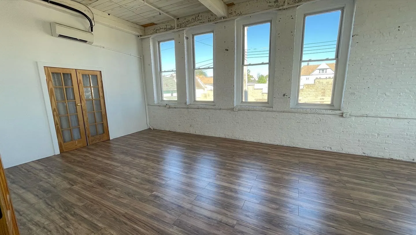 Studio wall of four windows with blue sky, wood floors and closet French doors