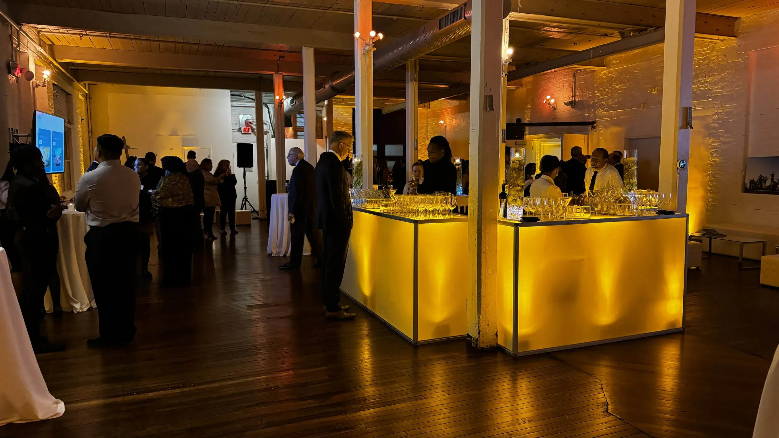 Guests gathered around the illuminated cocktail bar between brick walls and columns