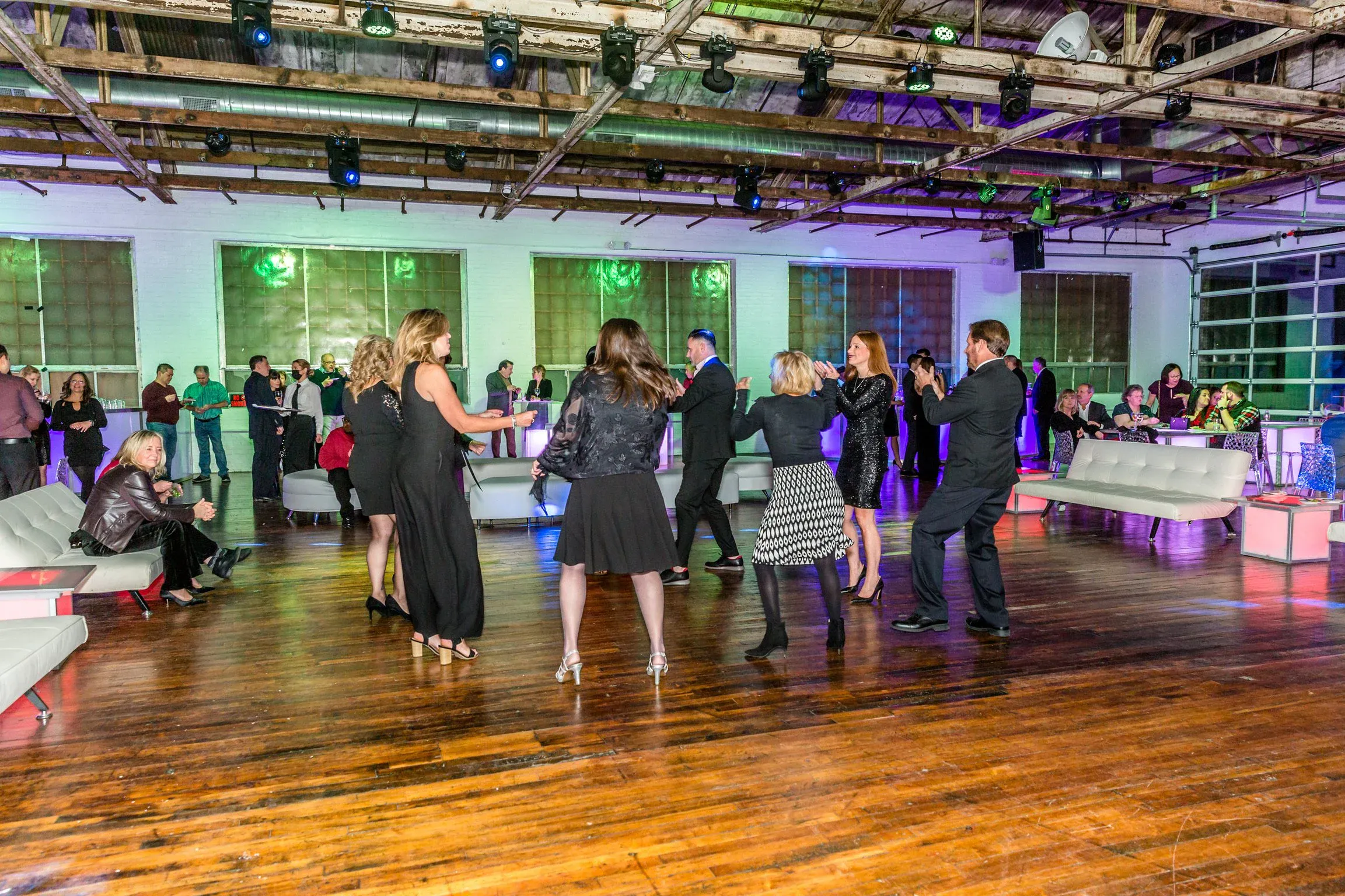 Guests in cocktail attire dancing in a circle under colorful uplighting