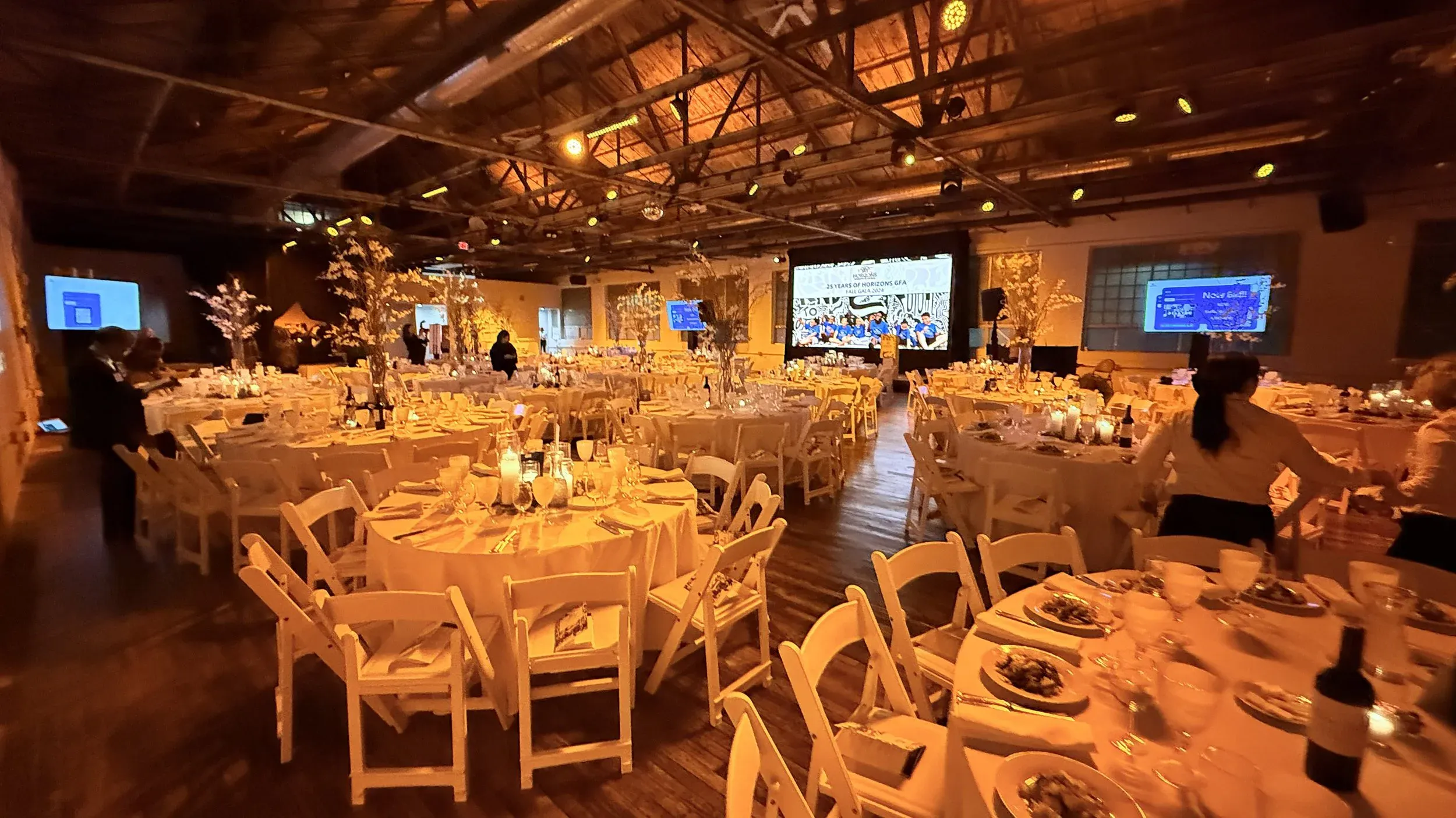 Corporate gala dinner room set with round tables under string lighting and timber trusses