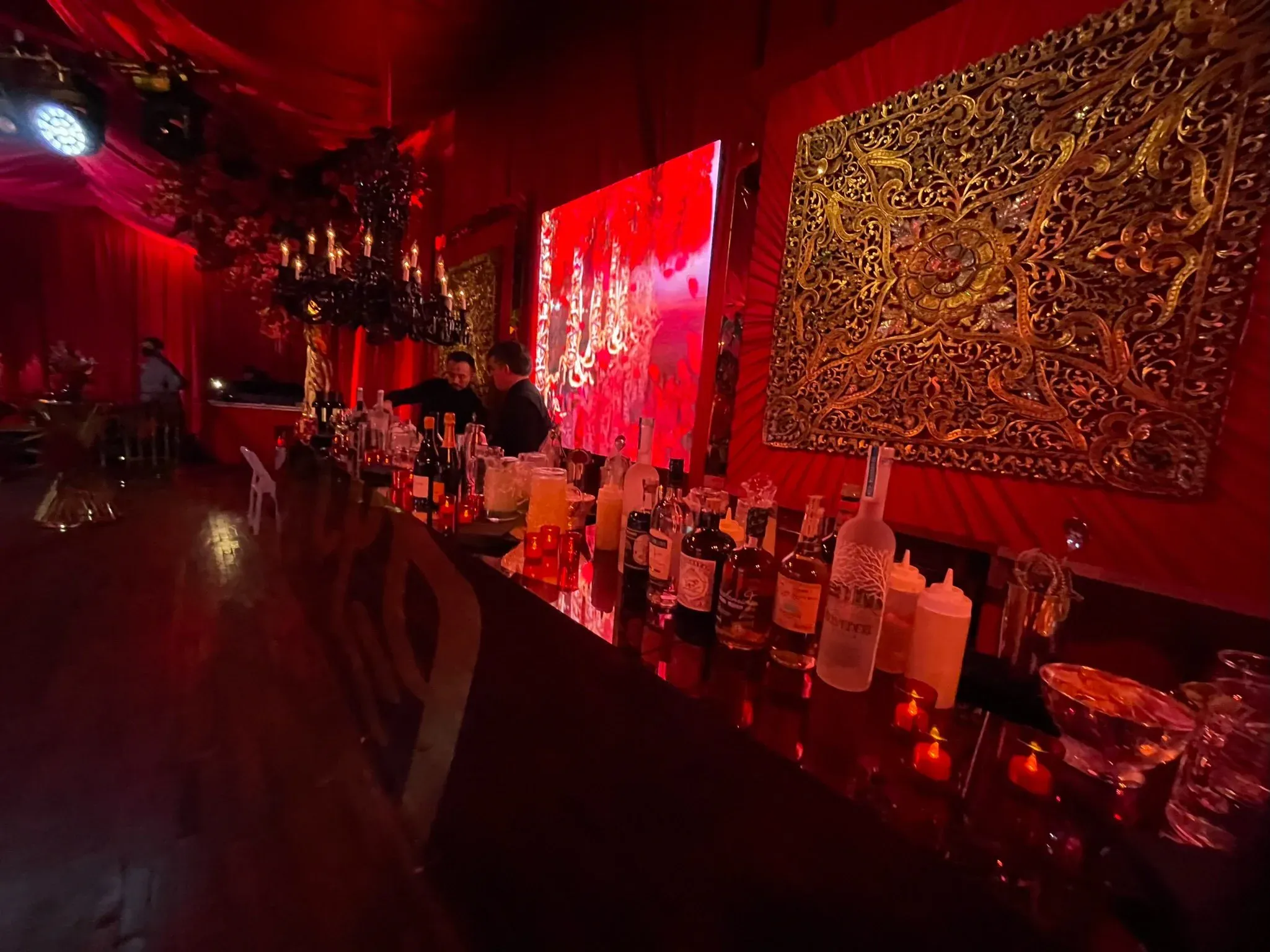 Moody red-lit lounge bar with ornate gold wall art and candles
