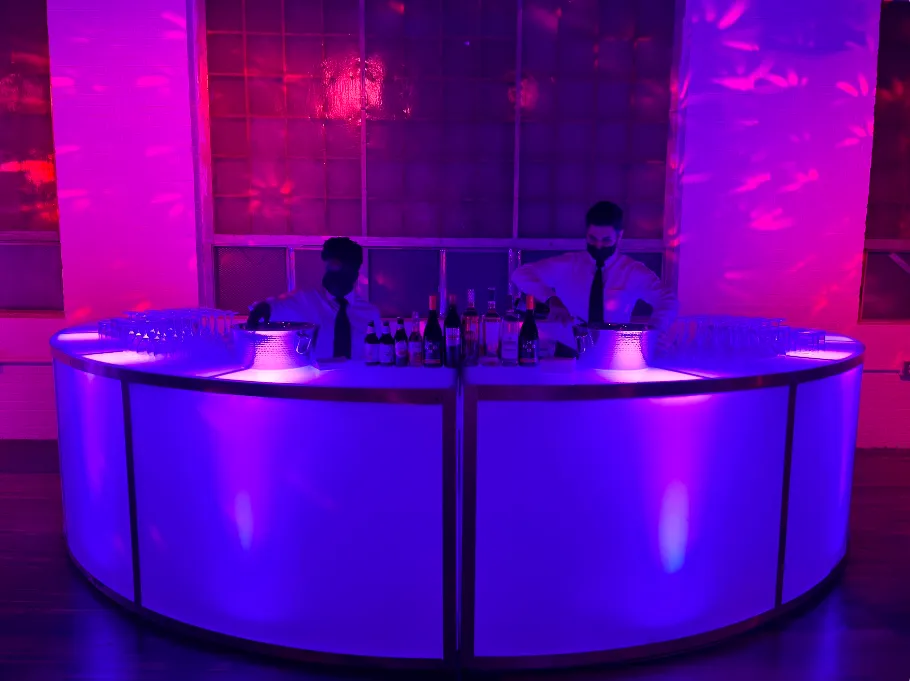 Two bartenders behind an illuminated bar serving a corporate event crowd