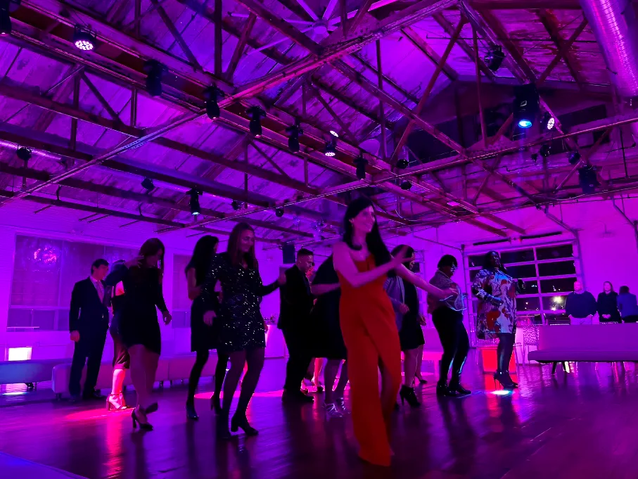 A packed dance floor at a corporate holiday party under the exposed wood truss ceiling at The Knowlton