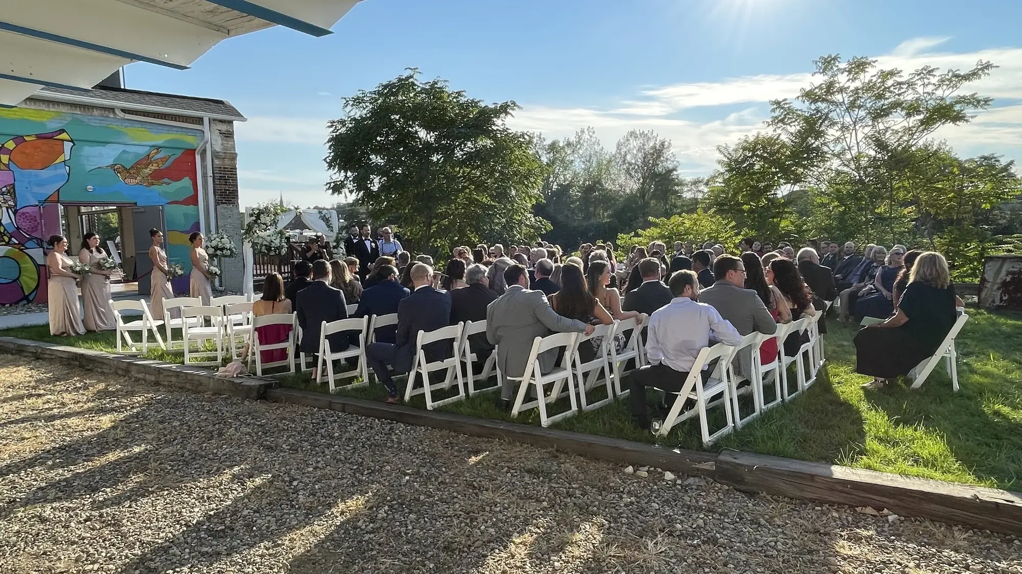 Outdoor wedding ceremony on the waterfront lawn inside the mural park, guests seated in white chairs