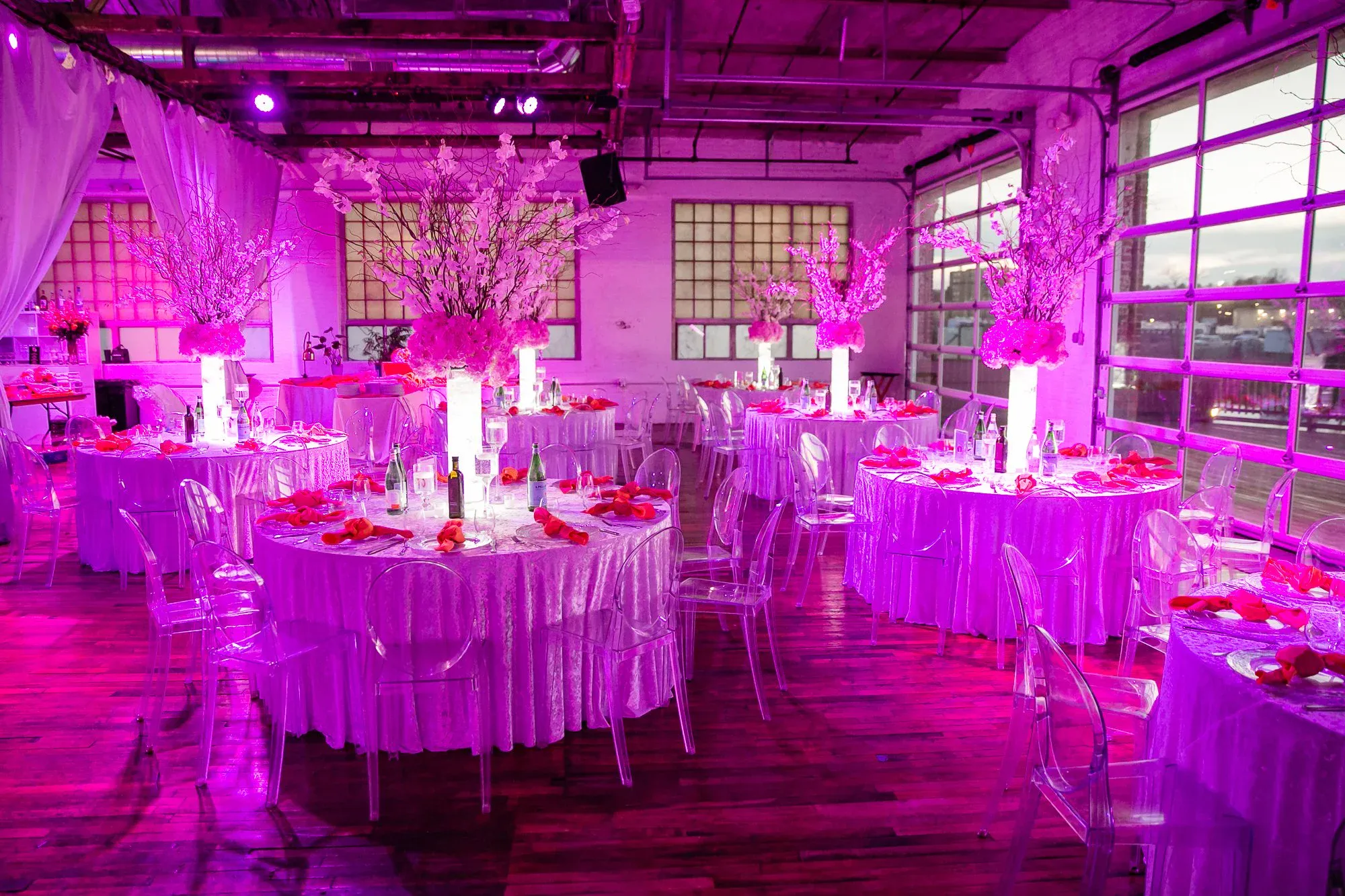 Pink-lit mitzvah reception room with round tables and cherry-blossom centerpieces